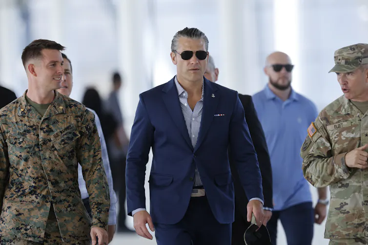 Pete Hegseth walks alongside two men in army attire.