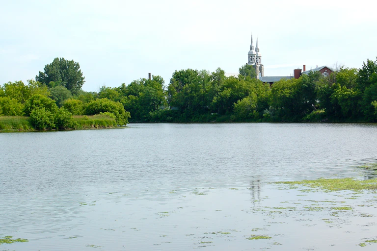 Une rivière bordée par de la végétation et une église au loin