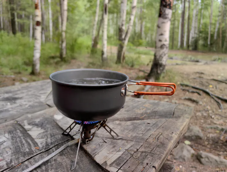 Steaming pot of water on small portable stove on top of a plank of wood in a forest