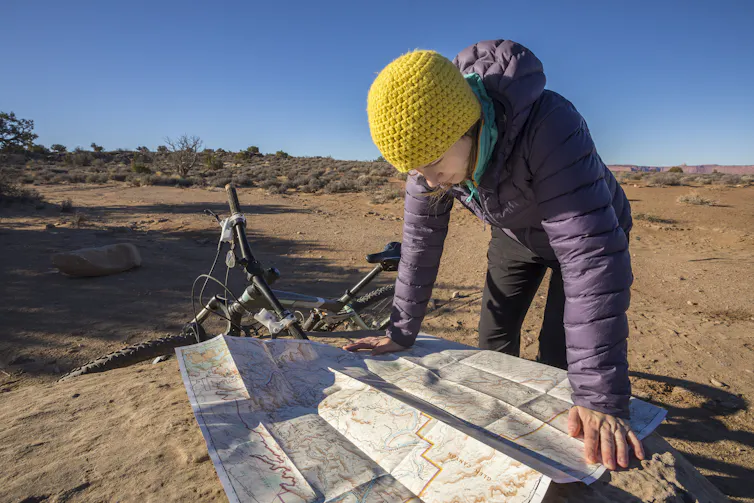 Person leaning over map spread over a rock beside a bike, plains stretching into the background