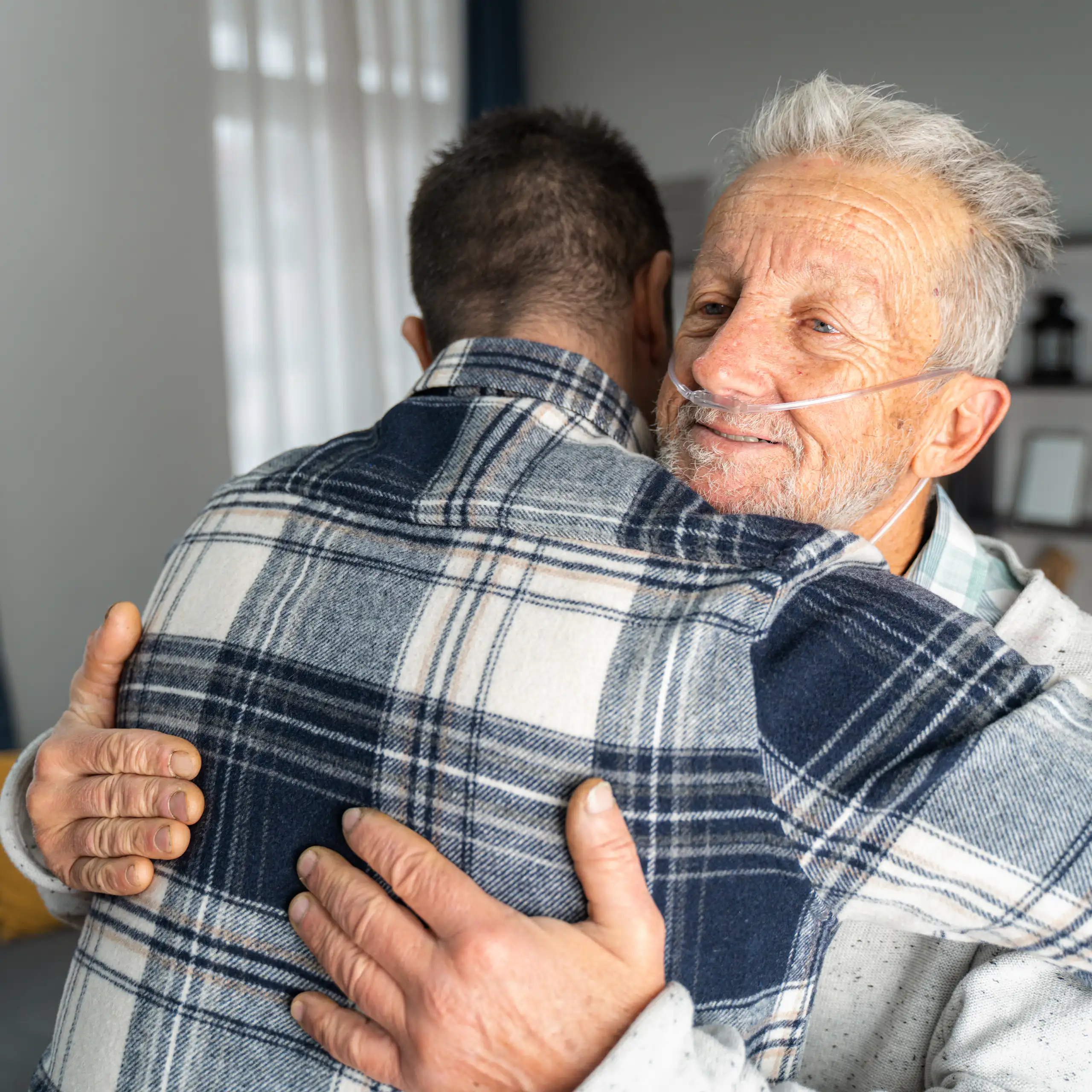 Older man with oxygen tubes in nose embraces son.