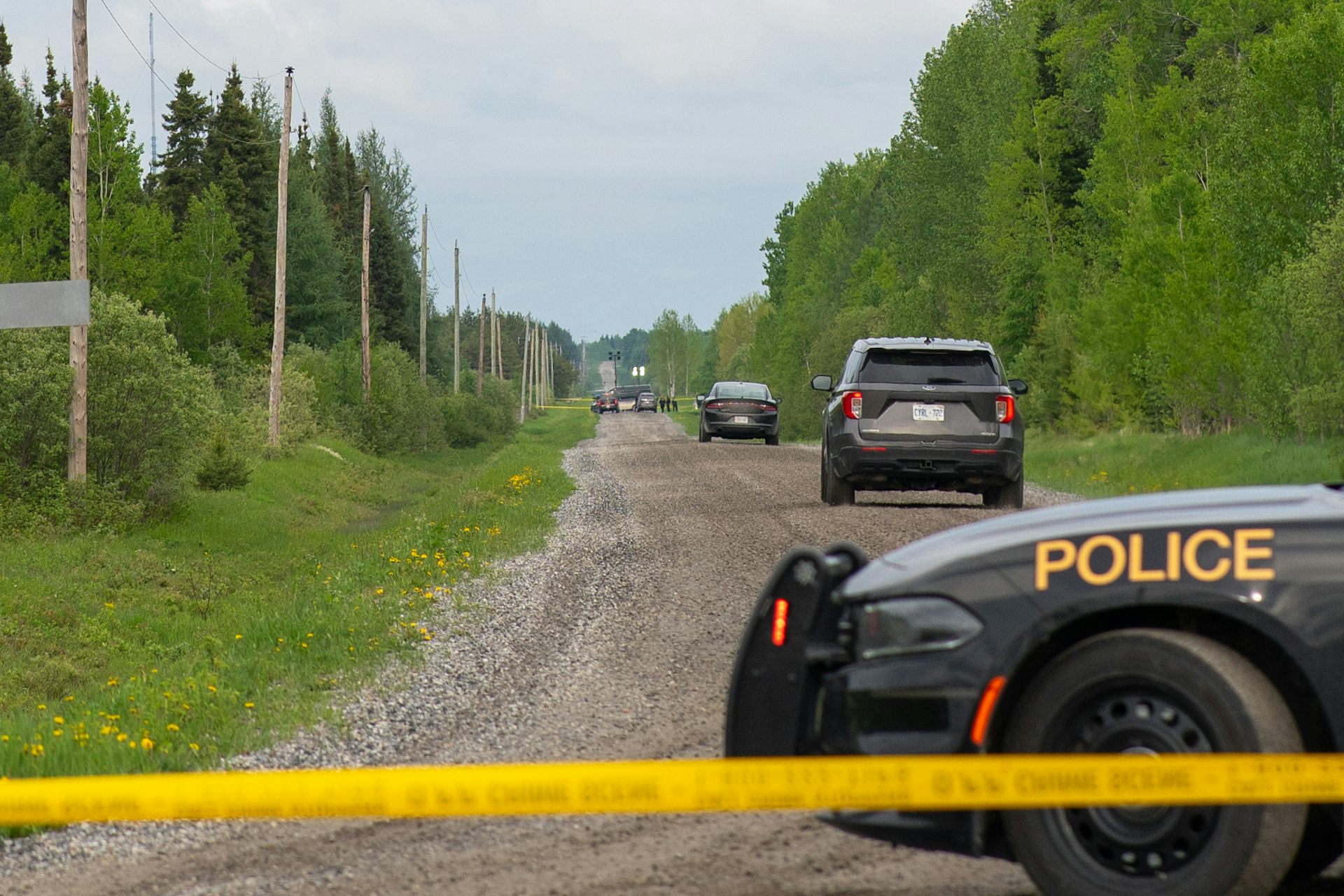 Three police cruisers on a rural road behind yellow police tape.