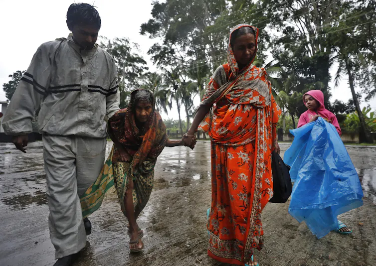 family of four bangladeshi people holding bags escaping cyclone