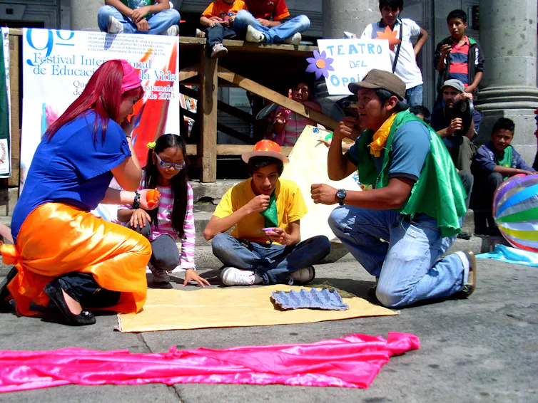 Varias personas rodeadas de carteles discuten, sentados en la calle, sobre un texto.