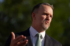 A man with short hair and a goatee gestures as he speaks outdoors.