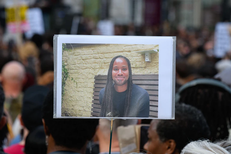 a placard showing a photo of jason arday being held in the air at a vigil held a few days after his death.