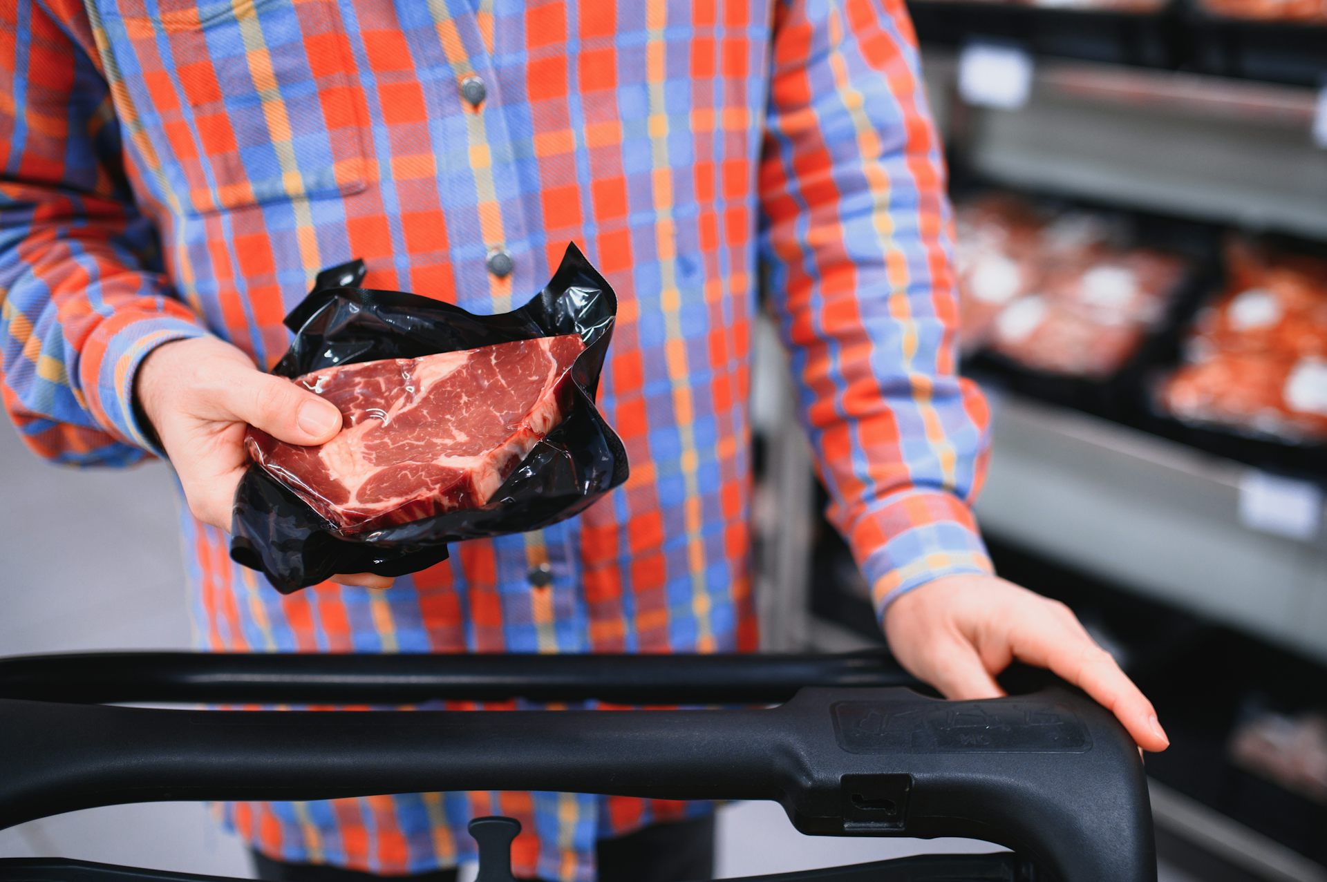 Dans un supermarché, un homme dépose un steak dans un caddy