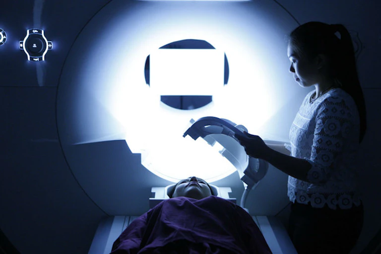 An advanced MRI scanner while an operator or researcher prepares a head coil for a brain imaging scan.