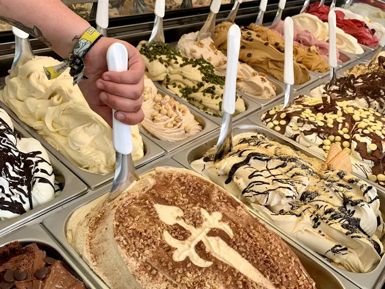 Diferentes helados en la vitrina de una heladería con sus paletas para echarlos