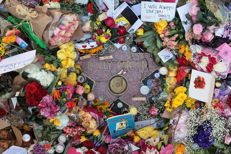 A heap of flowers, notes and photos lie on top of a star-shaped stone that says 'Dolly Parton.'