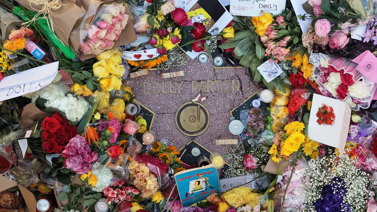 A heap of flowers, notes and photos lie on top of a star-shaped stone that says 'Dolly Parton.'