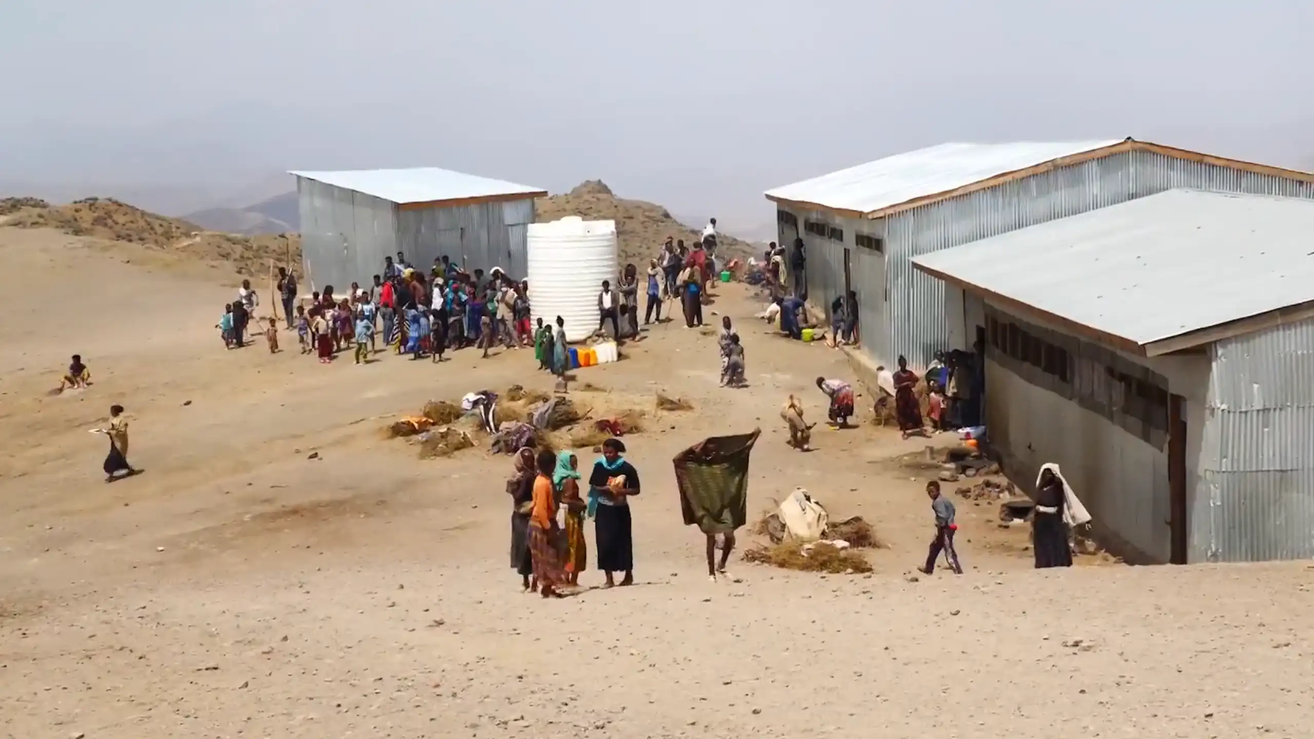 A group of people in a camp with makeshift homes made from iron sheets and built on sandy land.