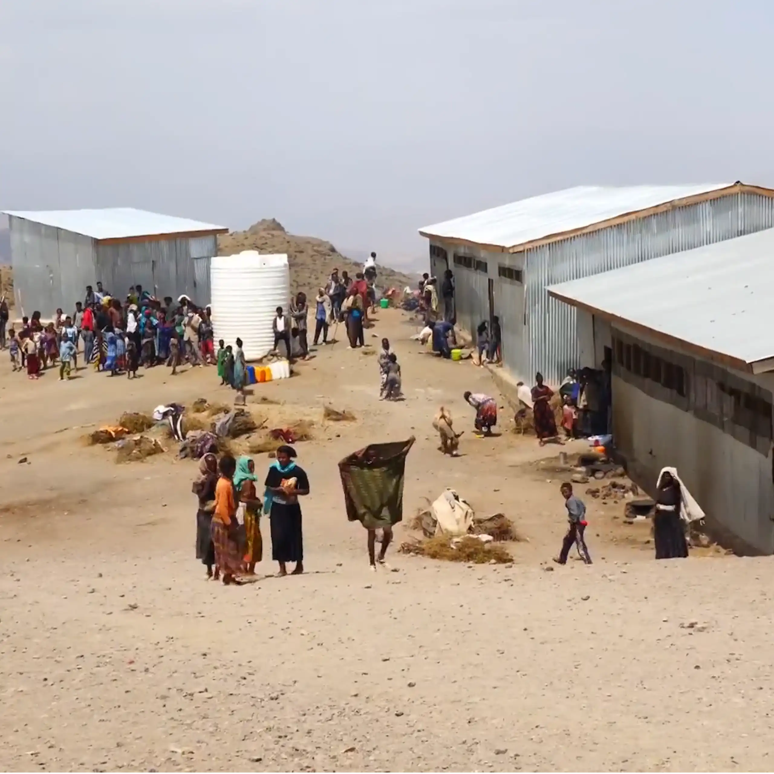 A group of people in a camp with makeshift homes made from iron sheets and built on sandy land.