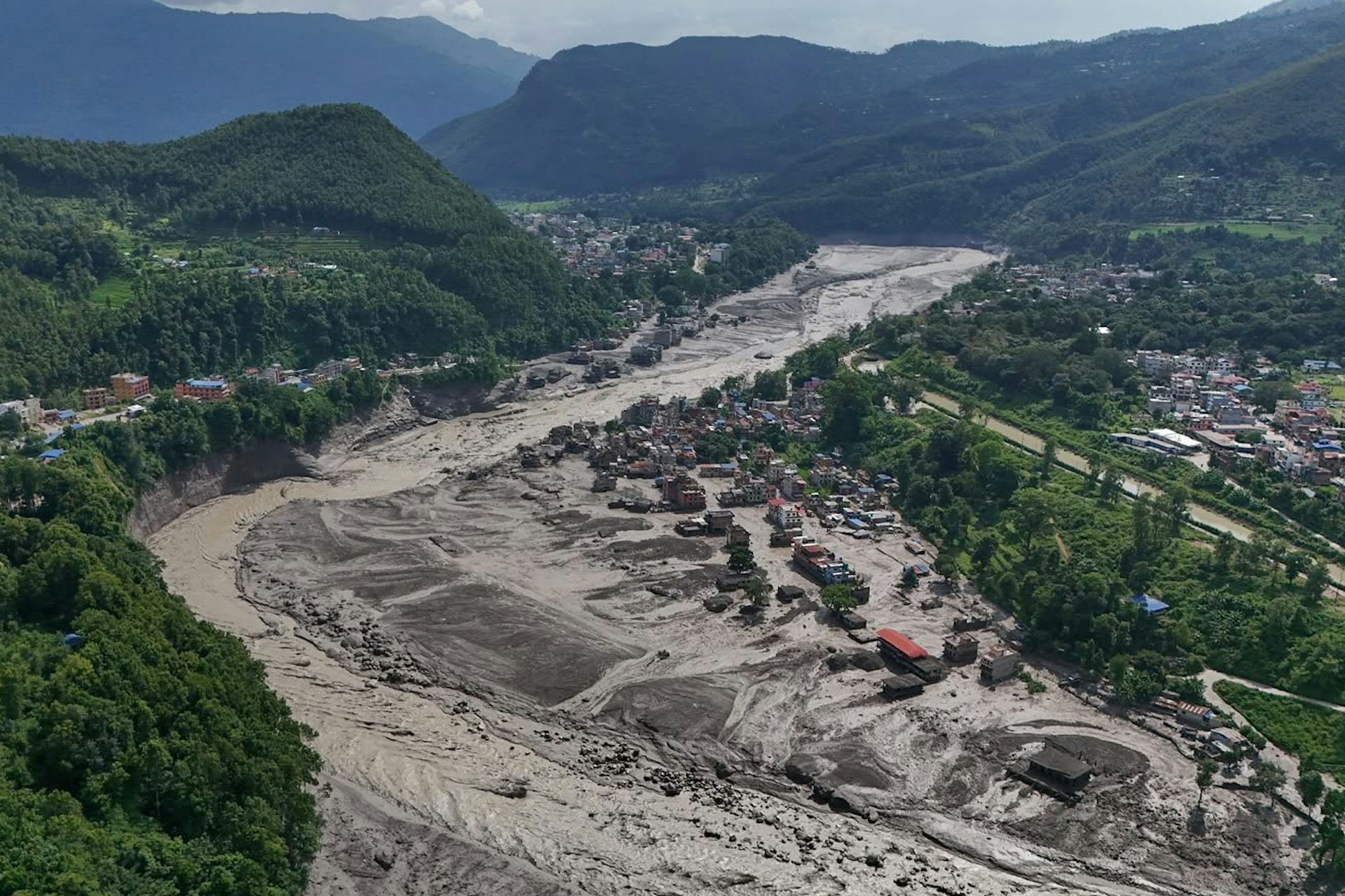 the aftermath of a flood in a town in a green hilled valley...a muddy river burst its banks, homes are surrounded by mud