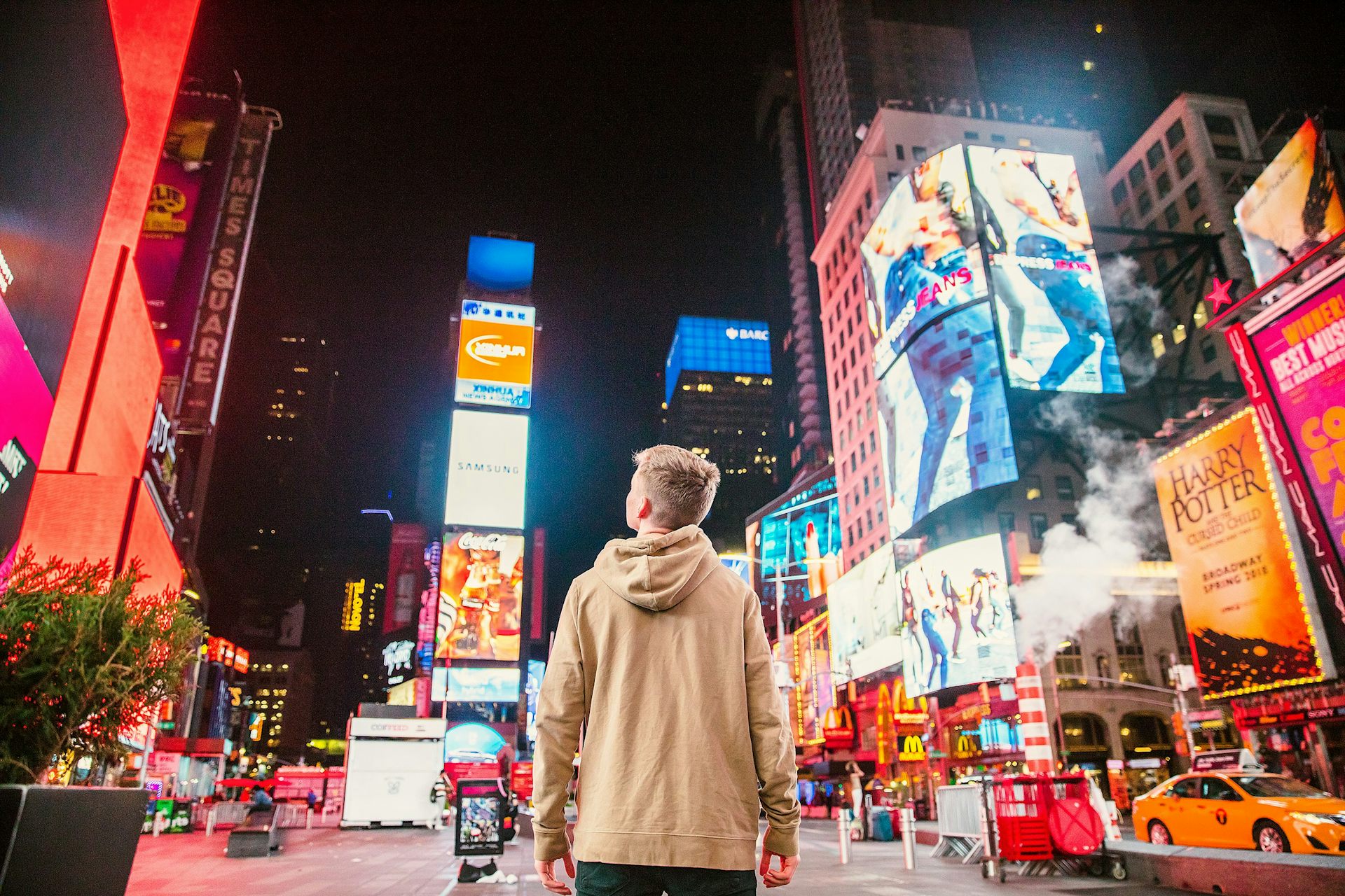 A young man stands in front of buildings lit up with advertising at night.