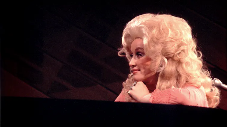 Woman with billowing, blonde hair gazes to her left while slyly grinning.