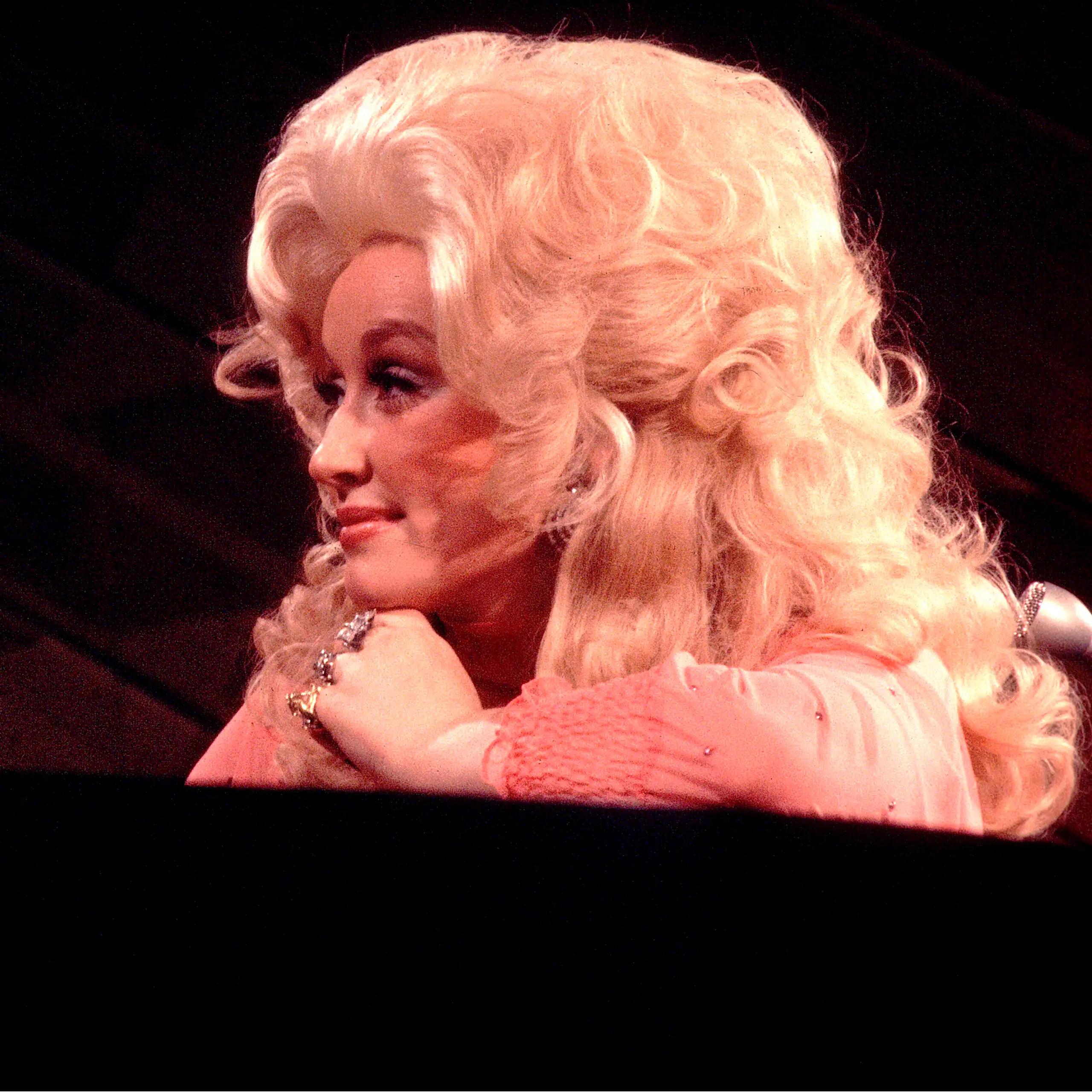 Woman with billowing, blonde hair gazes to her left while slyly grinning.