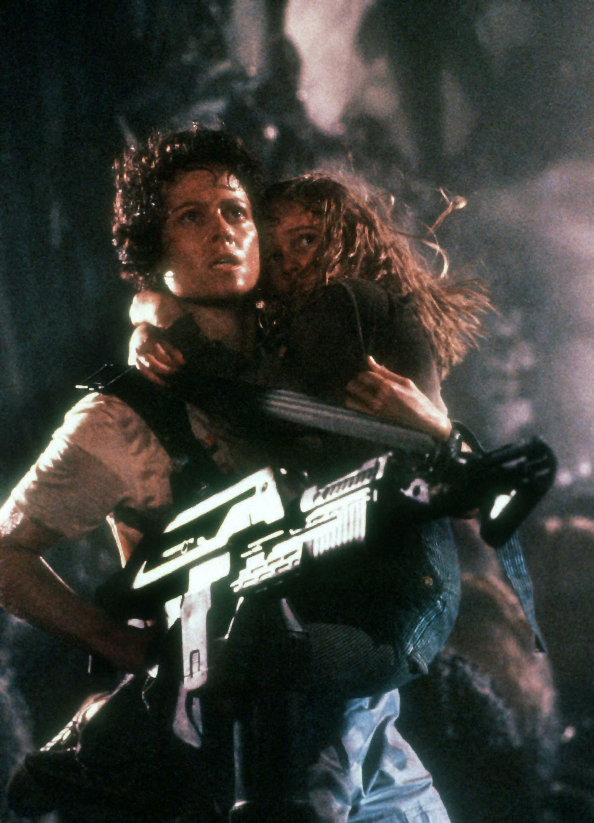 A woman holding a child and a huge automatic gun in a storm.