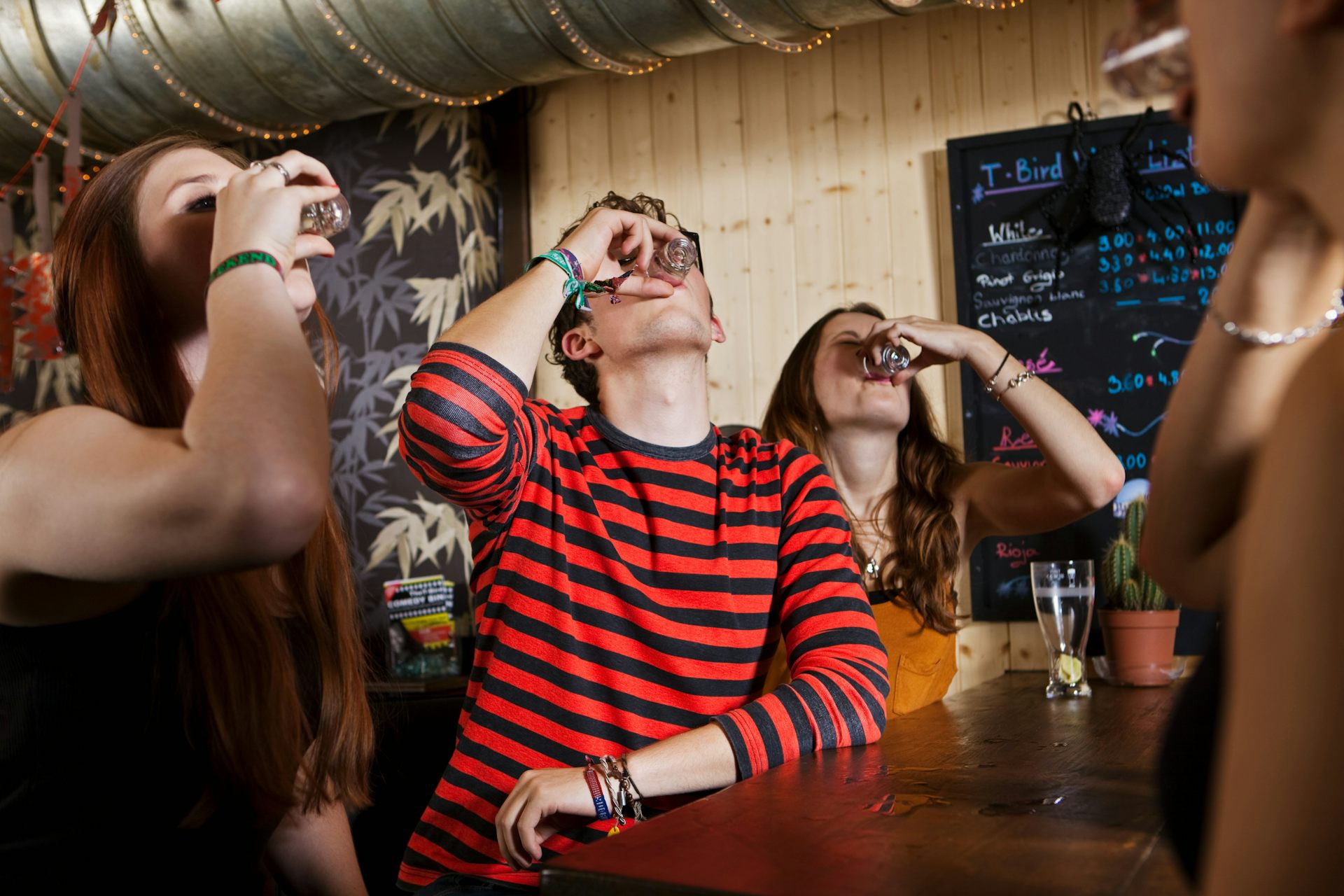 Four young people drink from shot glasses in a bar.