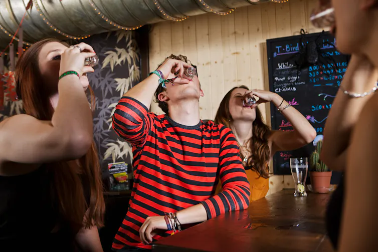 Four young people drink from shot glasses in a bar.