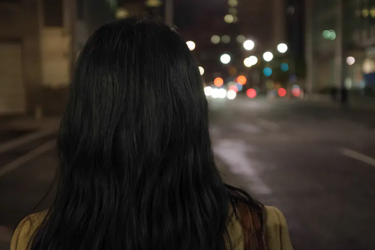 from behind shot of a woman walking down a city street at night.