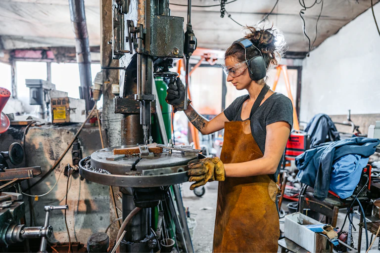 woman wearing ear protection works with drill press