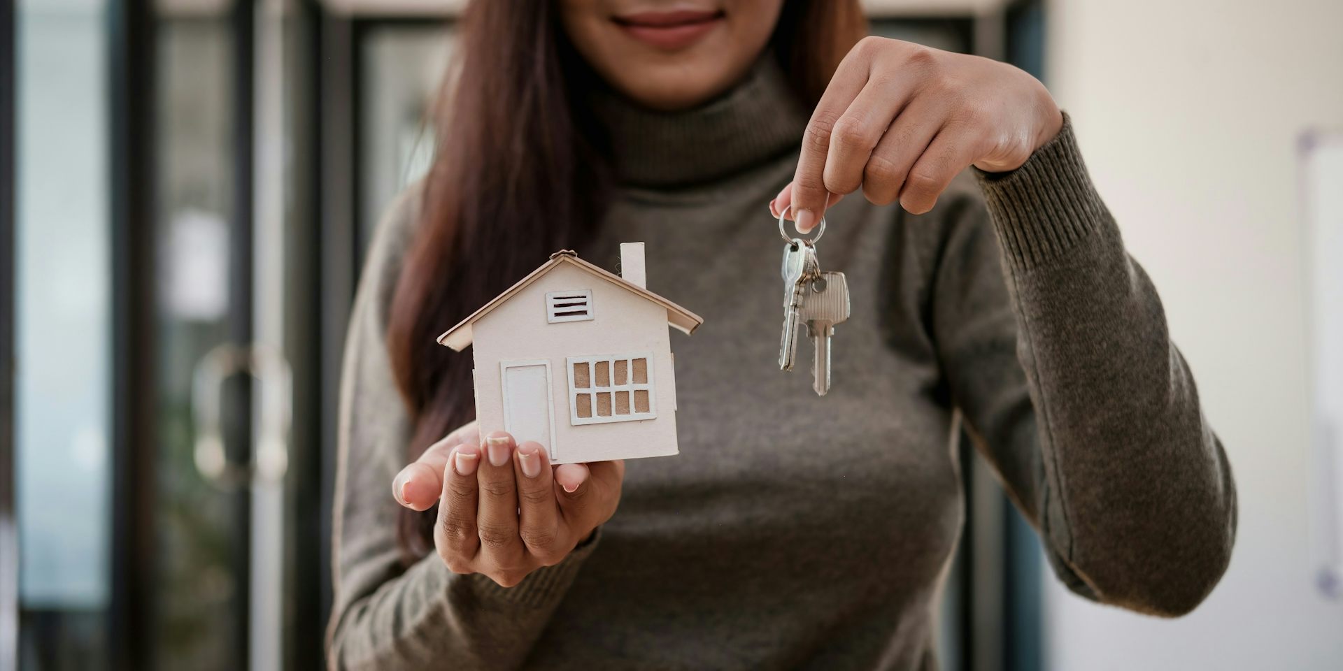 A close-up of a woman's torso while she holds a mock house and keys.