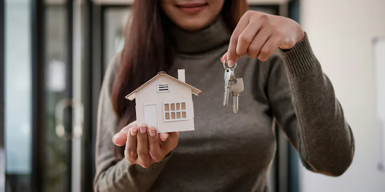 A close-up of a woman's torso while she holds a mock house and keys.