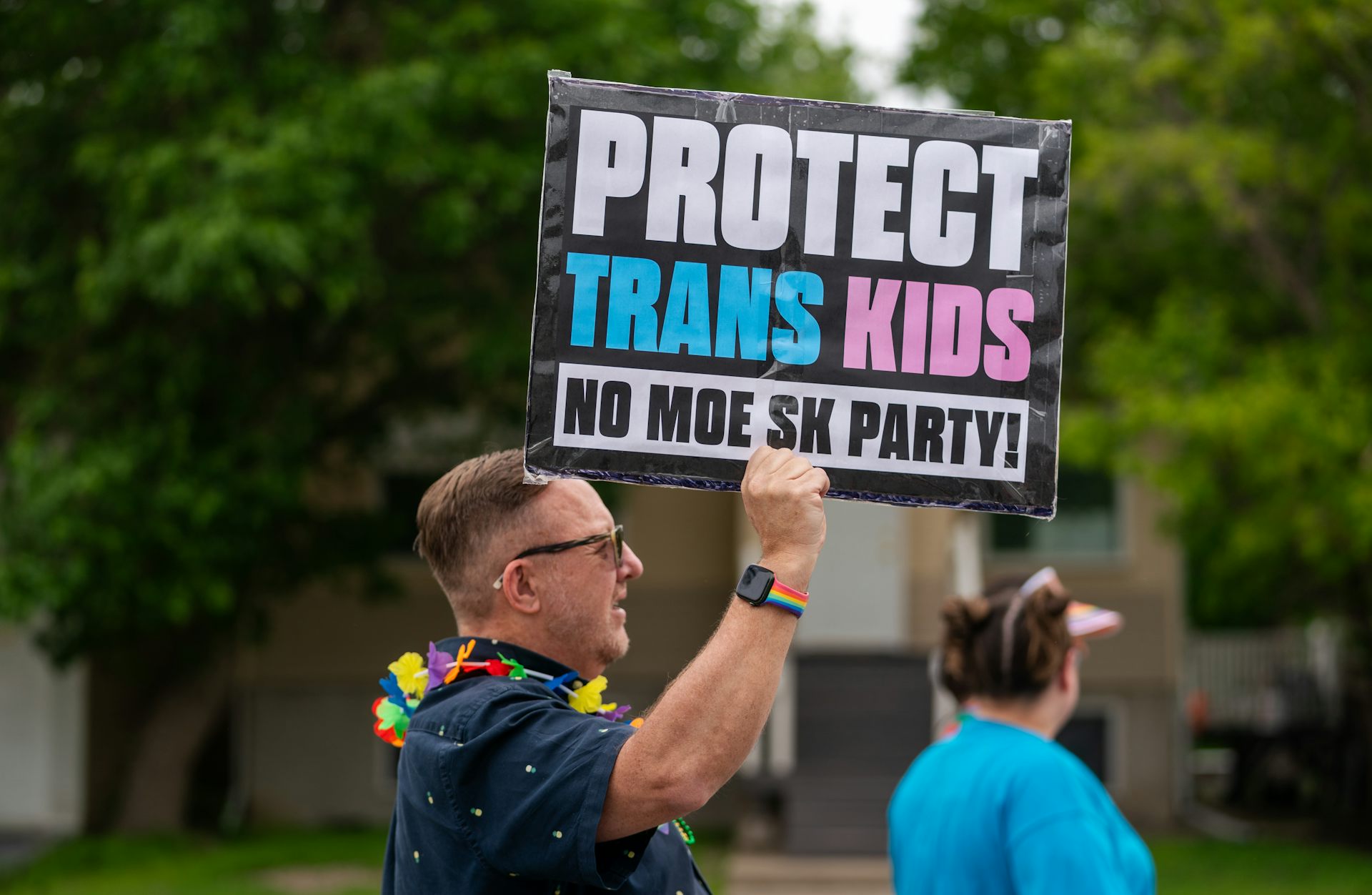 A person holds a pink and blue sign that says protect trans kids.