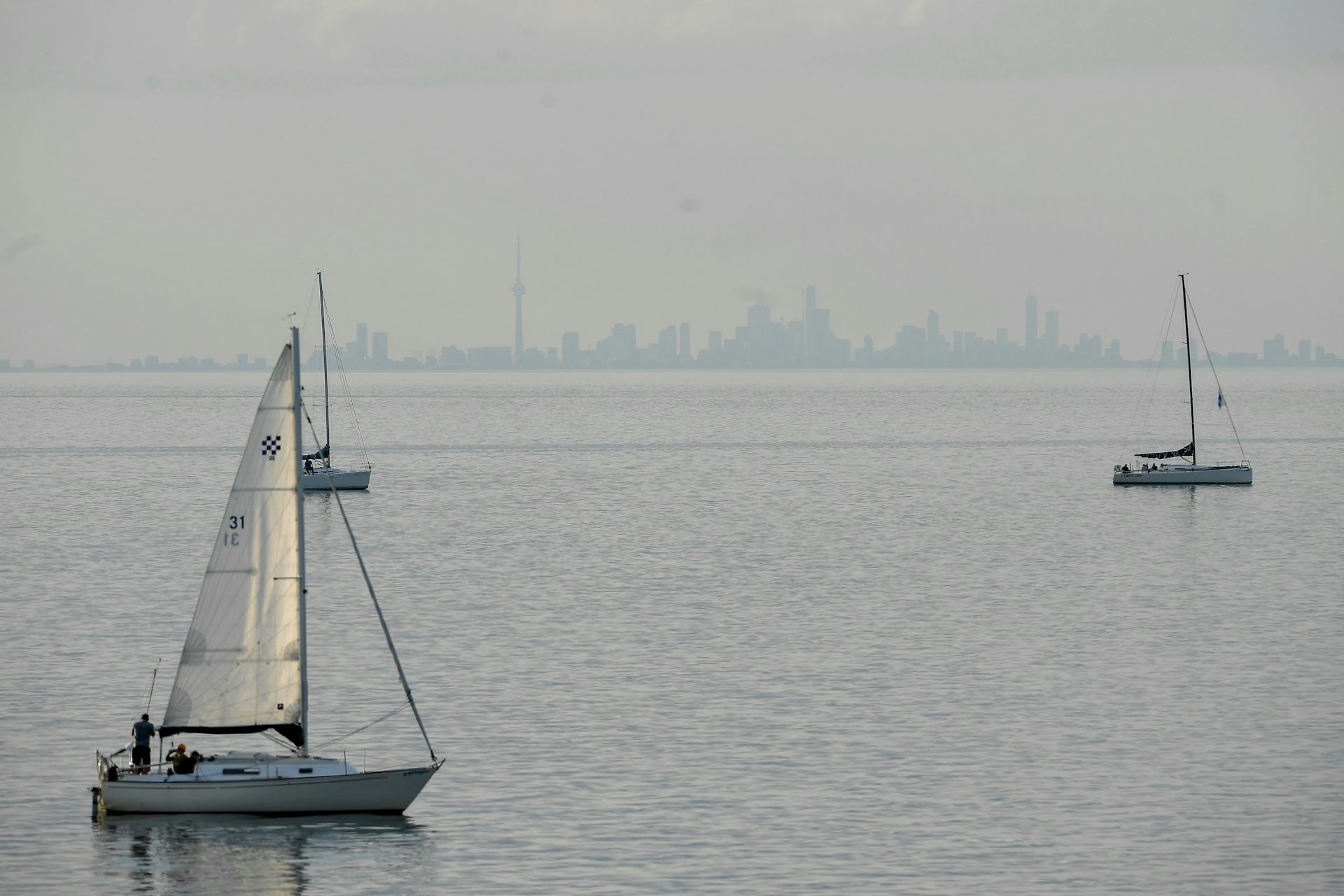 a city skyline seen in the far distance across a large lake, sailboats go across the water.