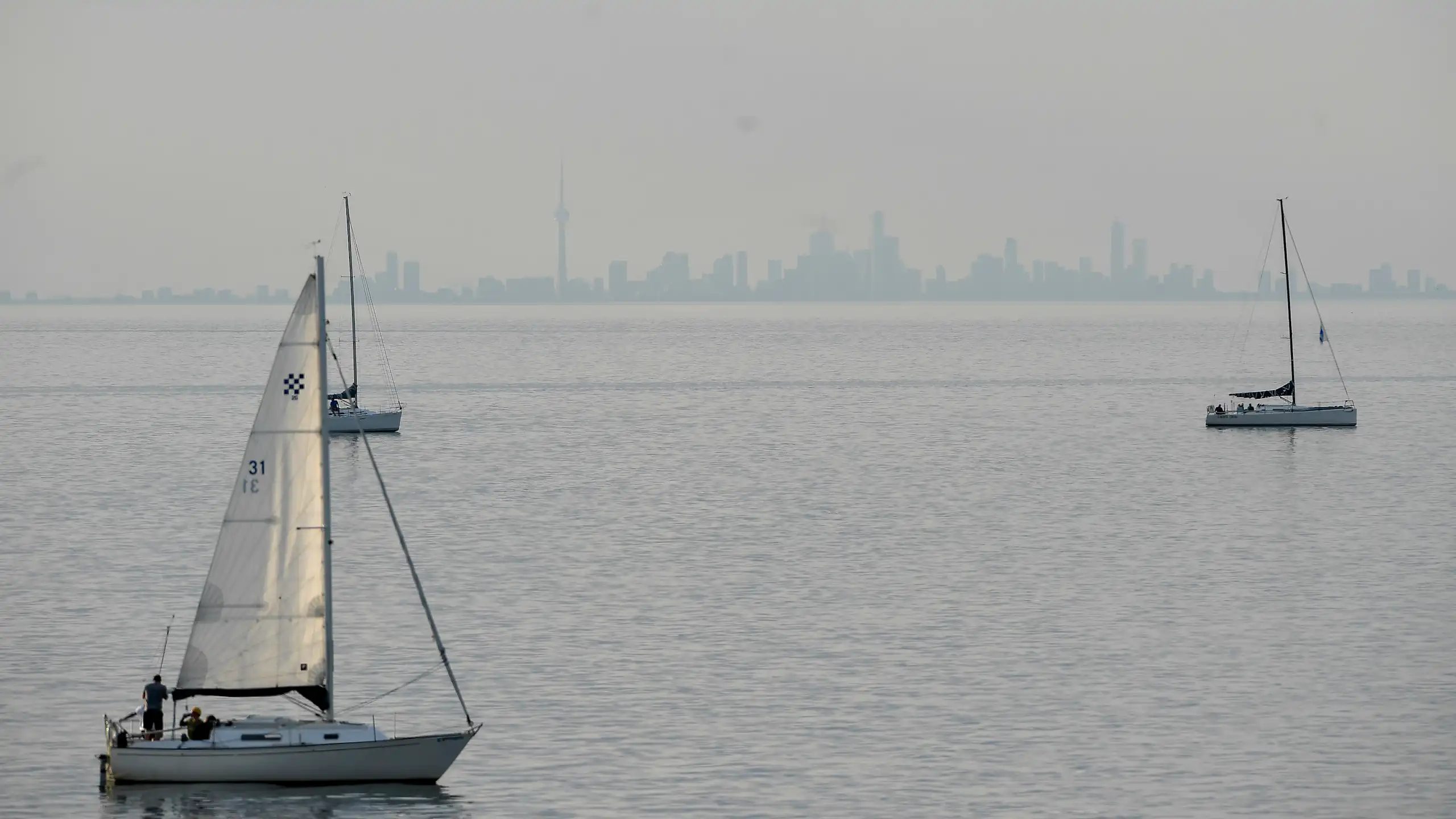 a city skyline seen in the far distance across a large lake, sailboats go across the water.