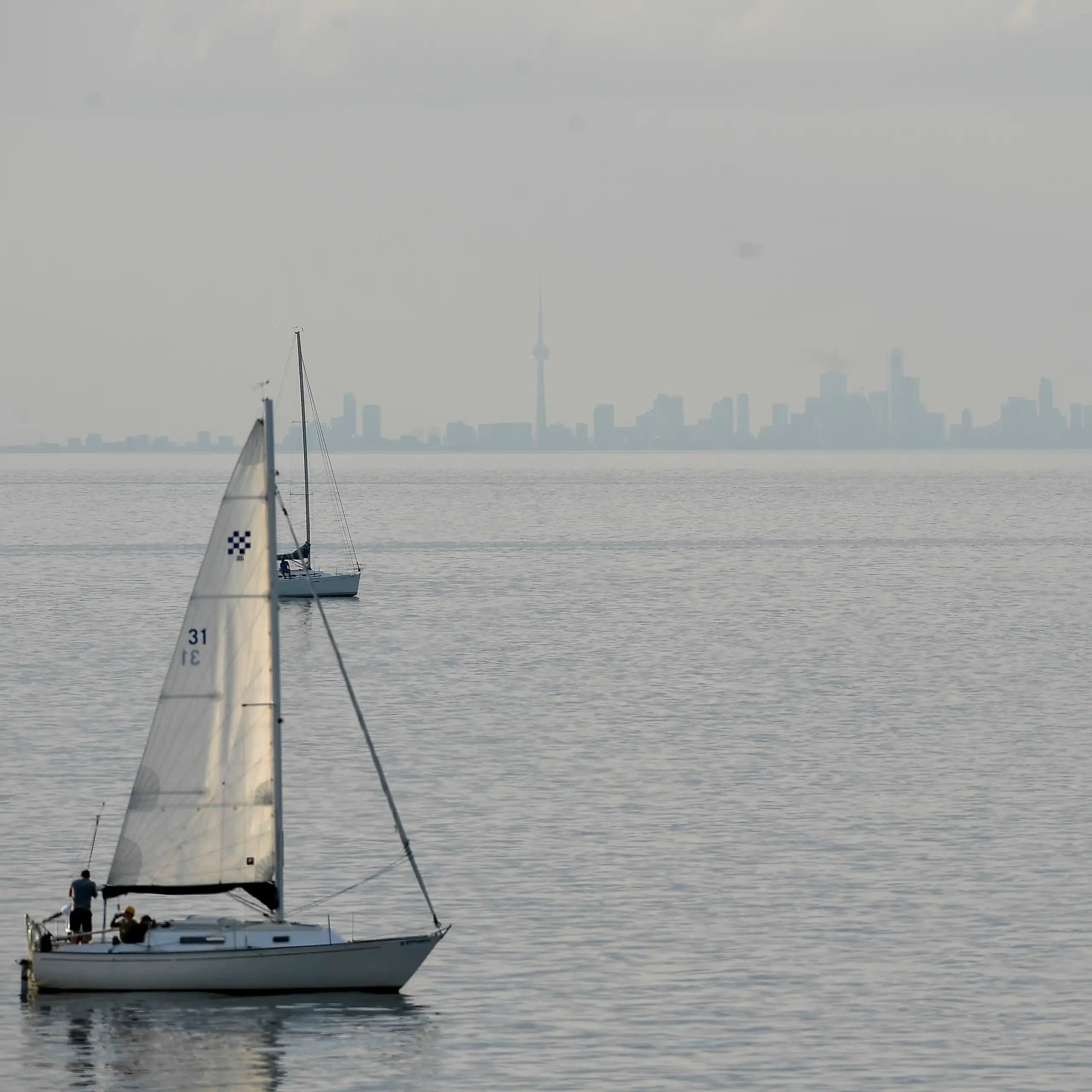 a city skyline seen in the far distance across a large lake, sailboats go across the water.