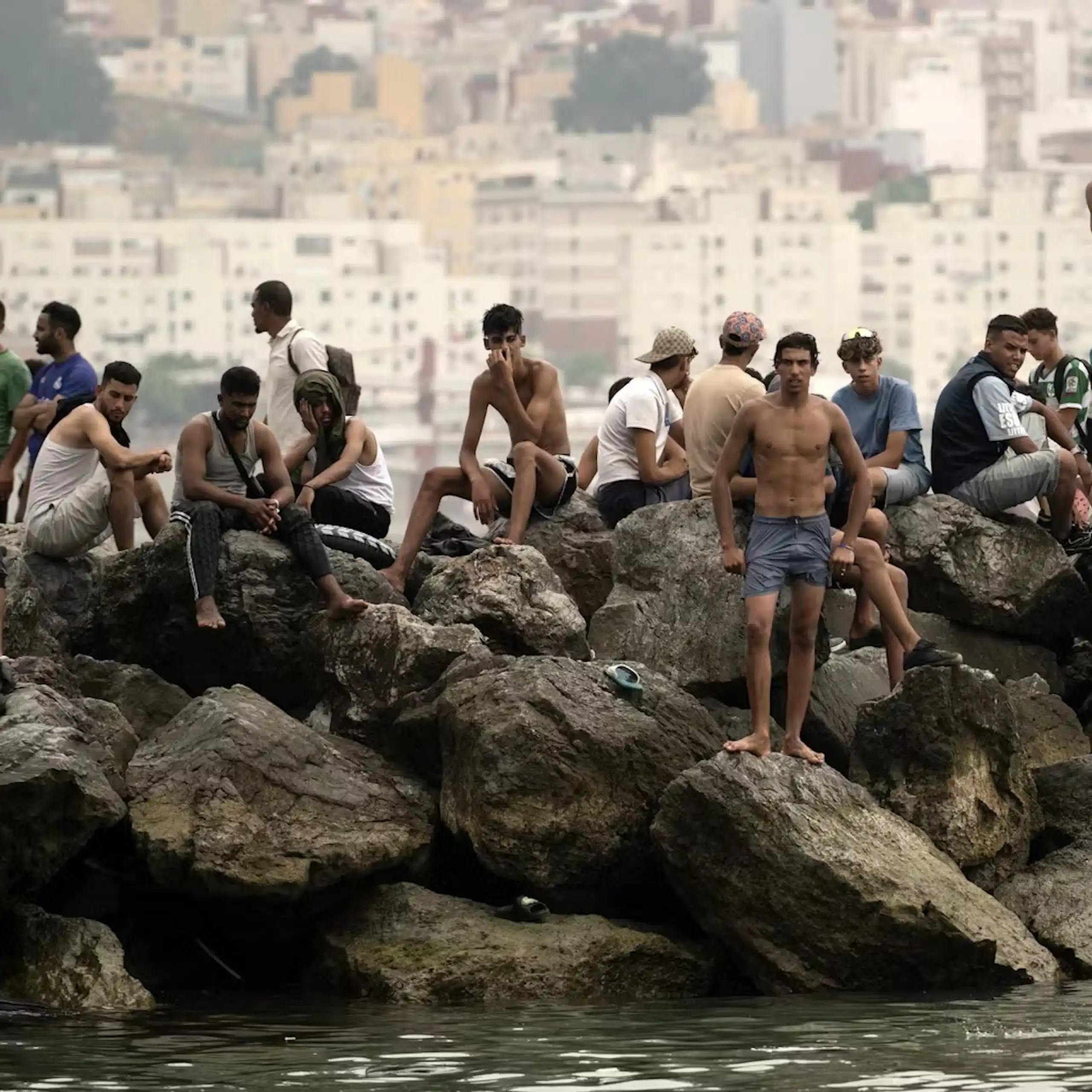 A group of men sitting and standing on rocks in a body of water