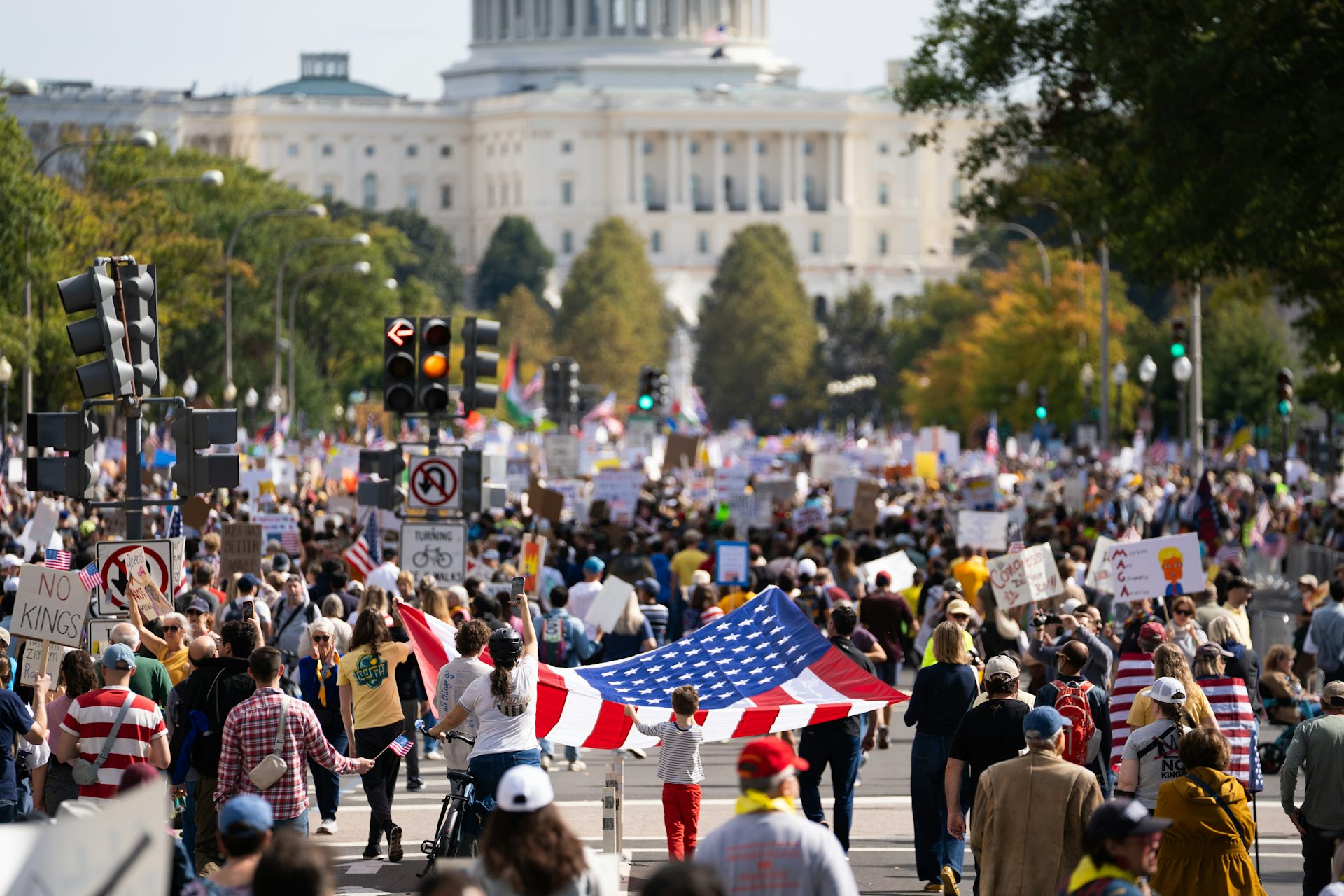 People walking with American flags on the street in front of a white-domed building.