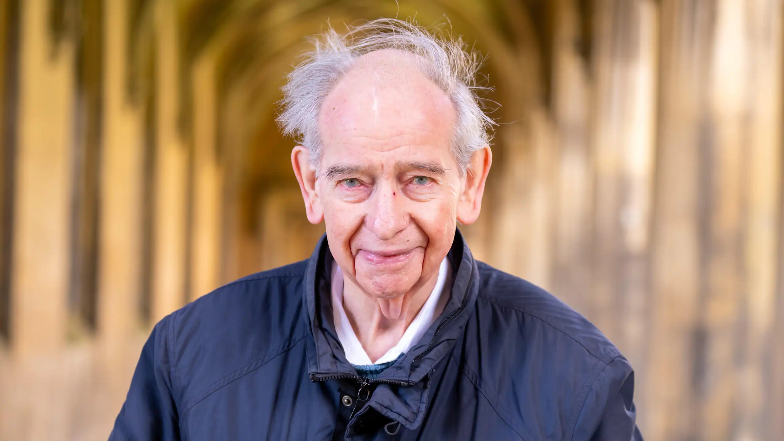 A man facing the camera, with a blurred hallway background