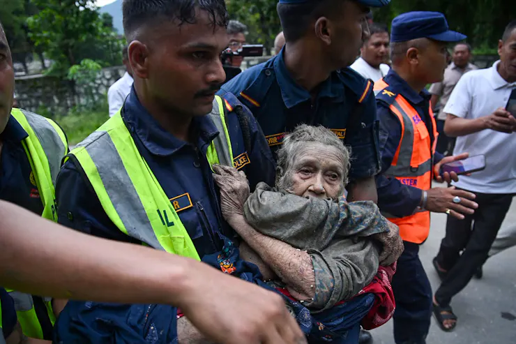 A line of rescuers carry a man covered in mud. He has a haunted look in his eyes.