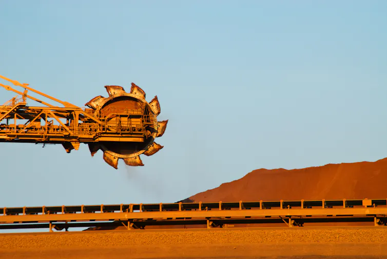 Mining machinery suspended above a red pile of iron ore.