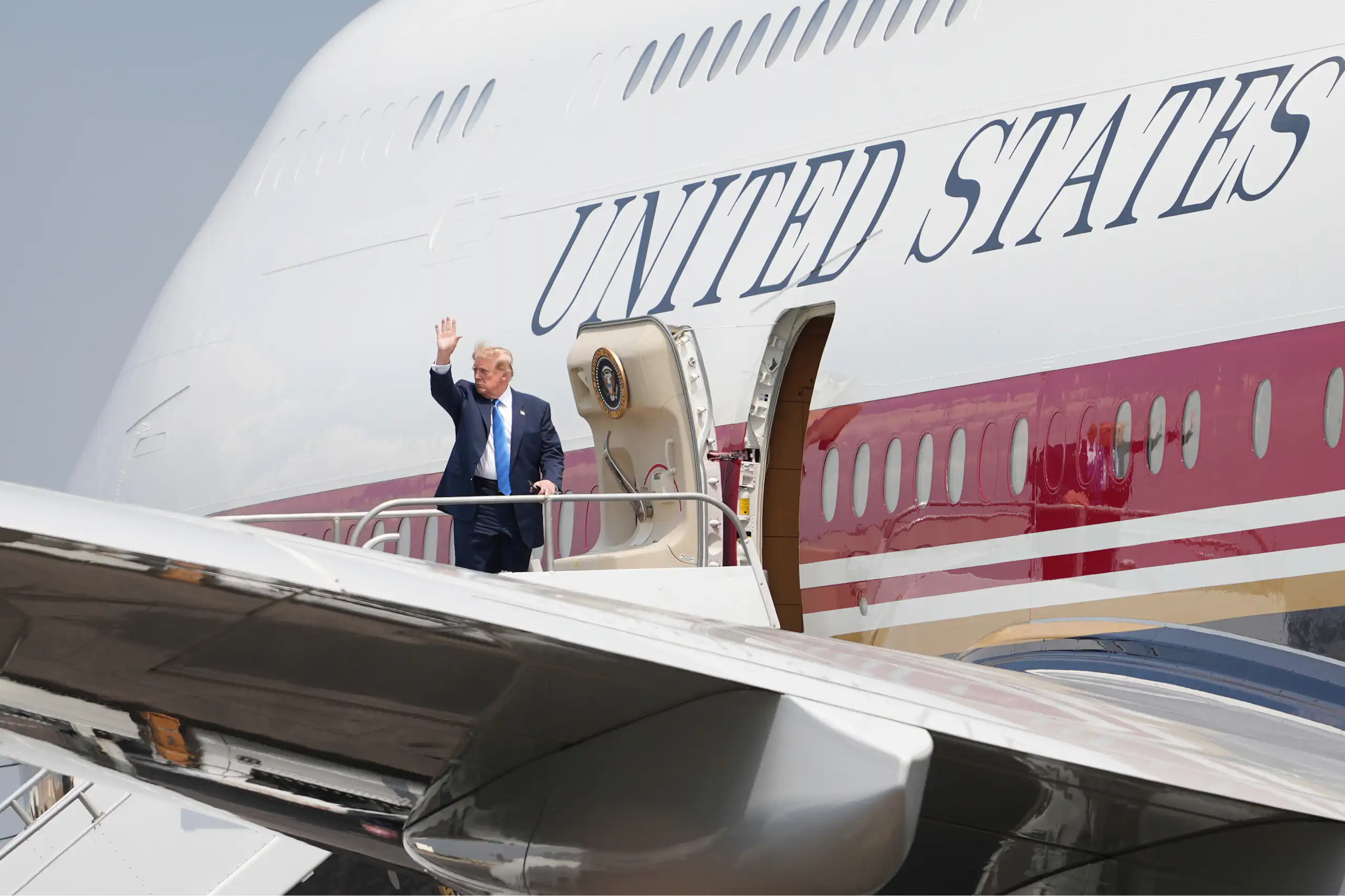 A rotund man waves as he gets into a large jet with United States emblazoned on its fuselage.