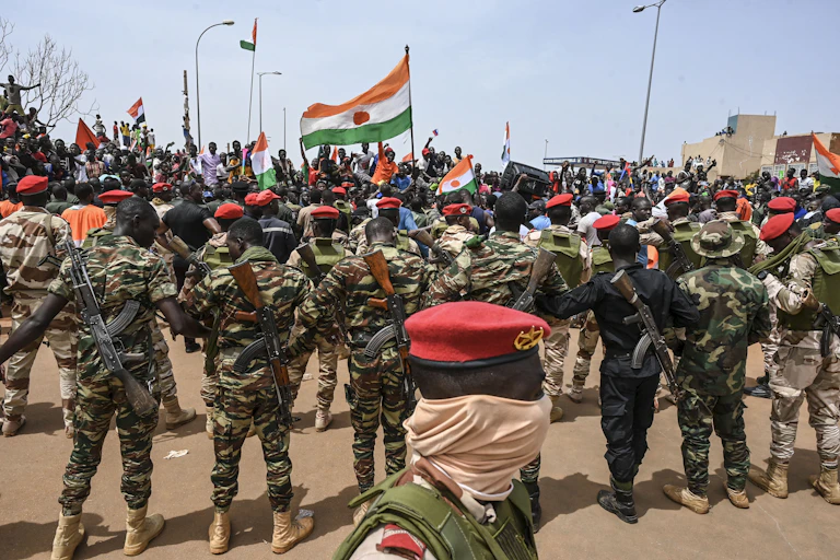 Soldiers in camouflage uniform, carrying weapons, and crowds in a street