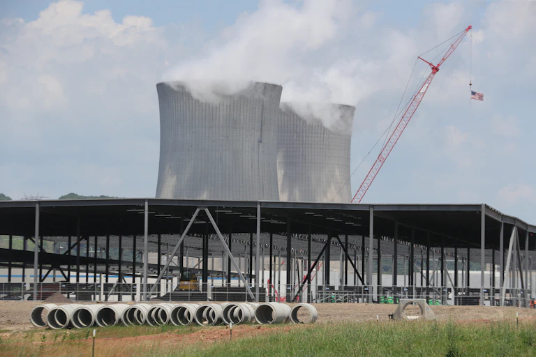 Two cooling towers releases steam in background and one-story structure of metal beams in foreground