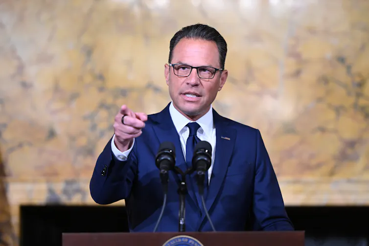 Man in blue suit speaks at podium and points finger