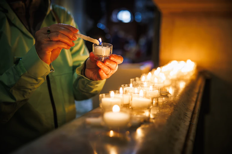 Una persona enciende una vela en una iglesia, para colocarla junto a otras ya encendidas