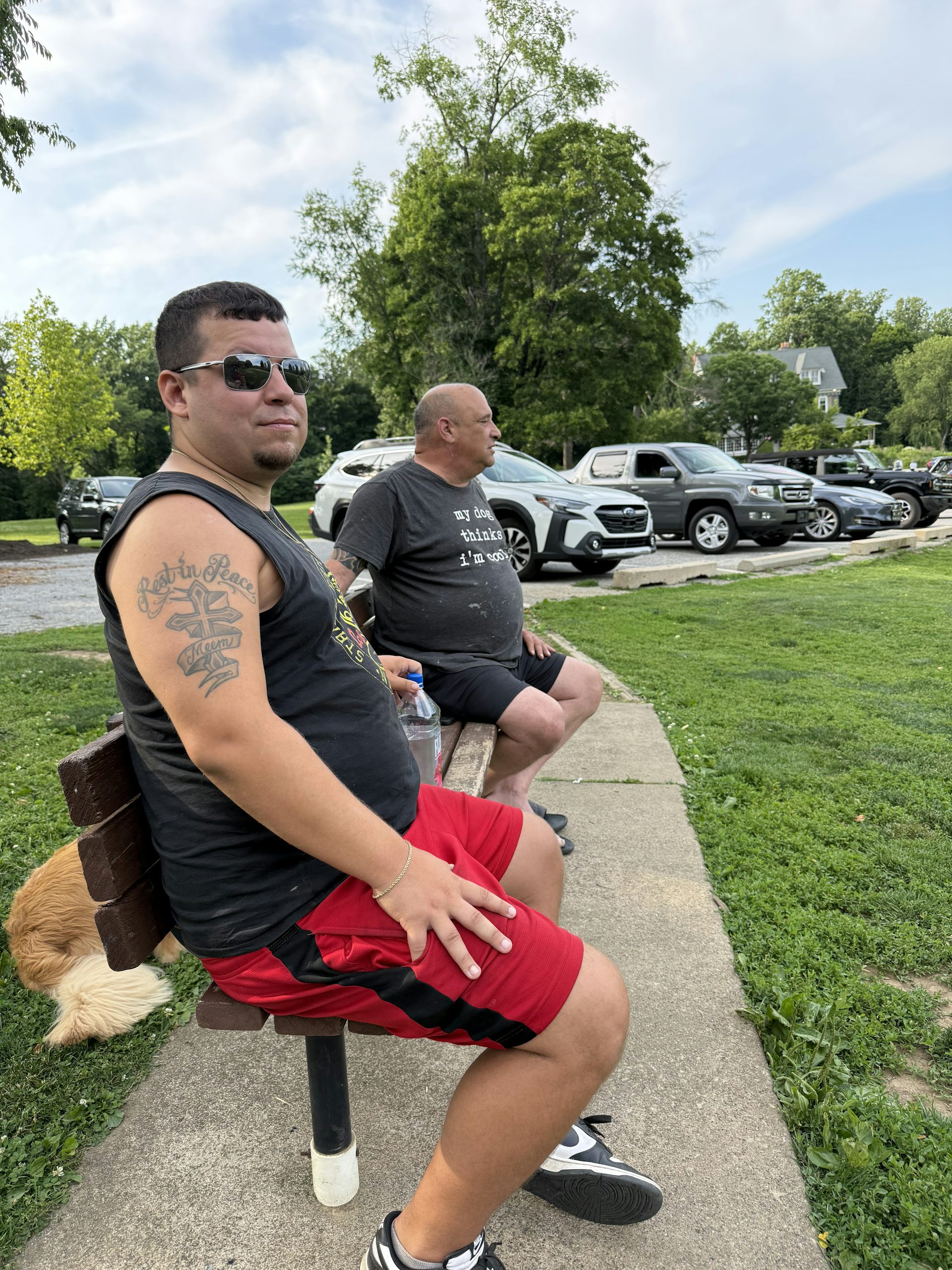 Two men sit on park bench with a dog behind them