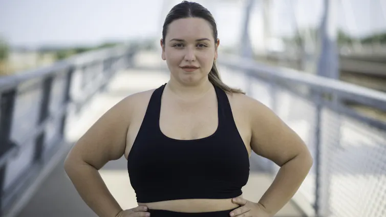 Woman wearing sportswear, standing confidently outdoors, looking directly at the camera, with hands on hips