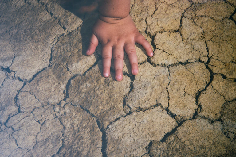 Child's hand on dry cracked earth in a heatwave