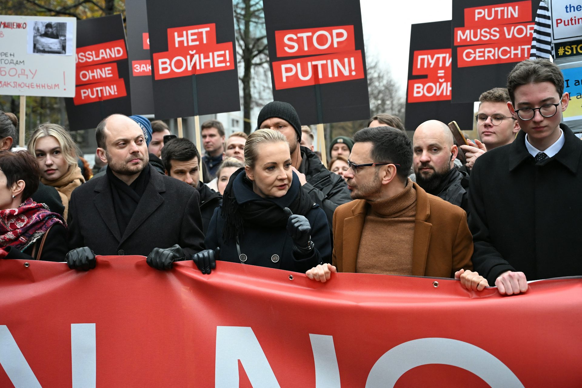 Photo de la rangée de tête de la manifestation, des pancartes « Stop Poutine », « Non à la guerre », en arrière-fond.