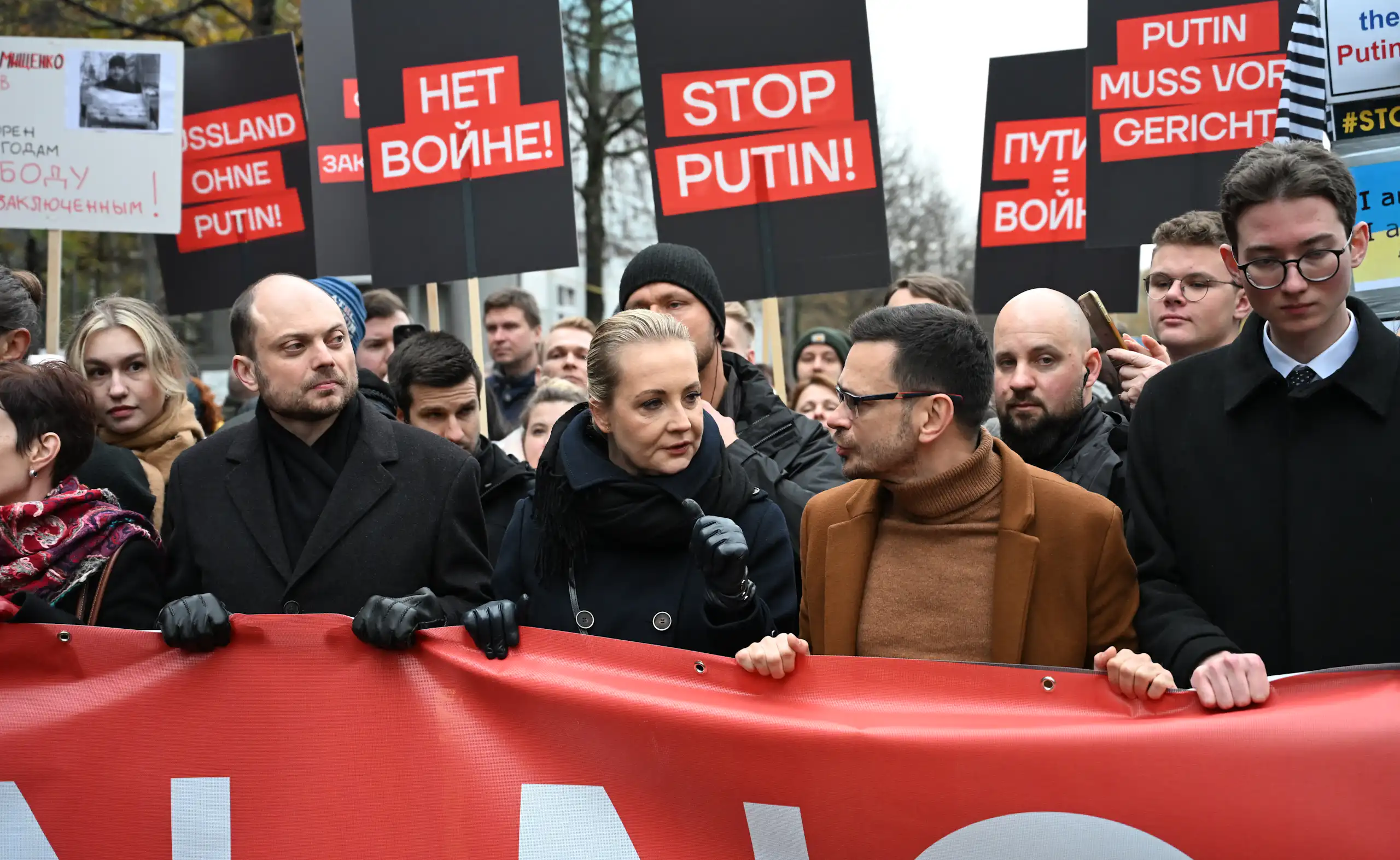 Photo de la rangée de tête de la manifestation, des pancartes « Stop Poutine », « Non à la guerre », en arrière-fond.