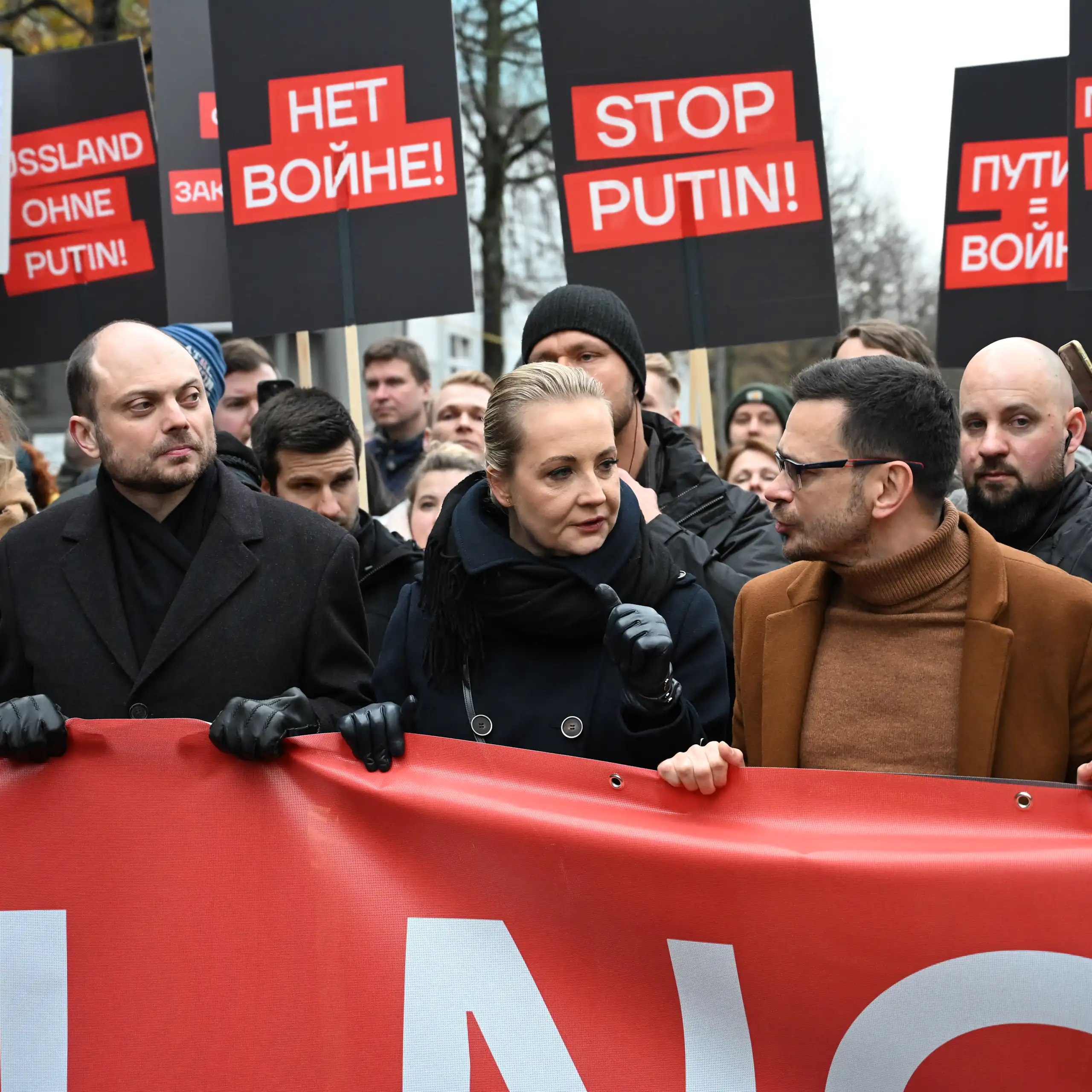 Photo de la rangée de tête de la manifestation, des pancartes « Stop Poutine », « Non à la guerre », en arrière-fond.