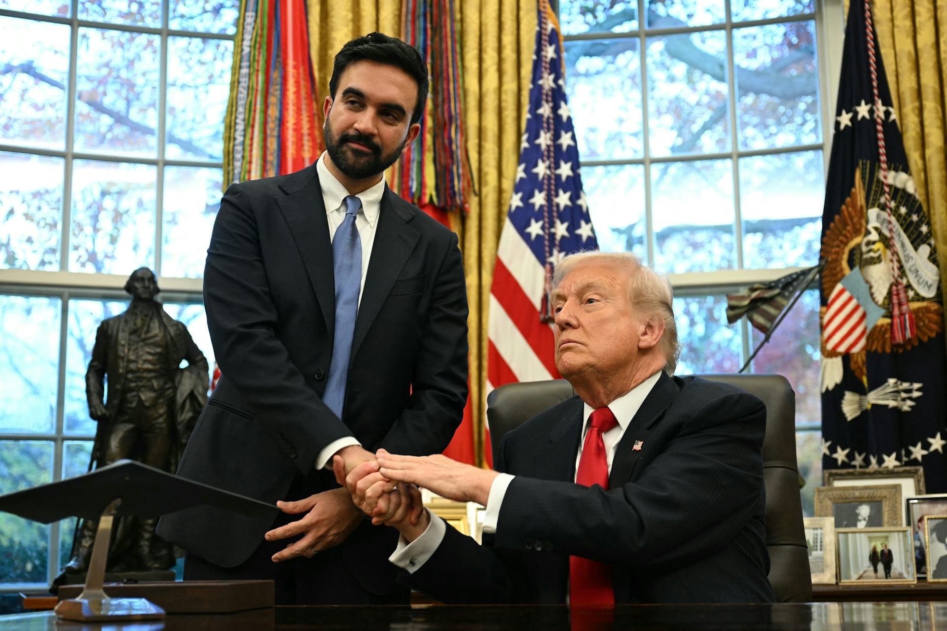 Donald Trump, ,assis à son bureau, serre la main de Zohran Mamdani, resté debout.