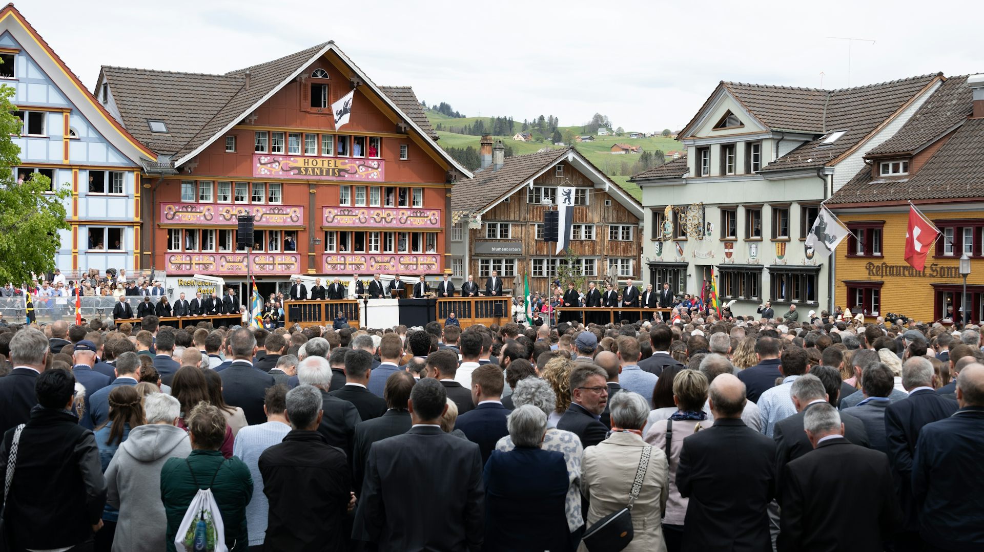 Foule assemblée sur une place, en arrière-plan, sur la tribune les conseillers du canton.